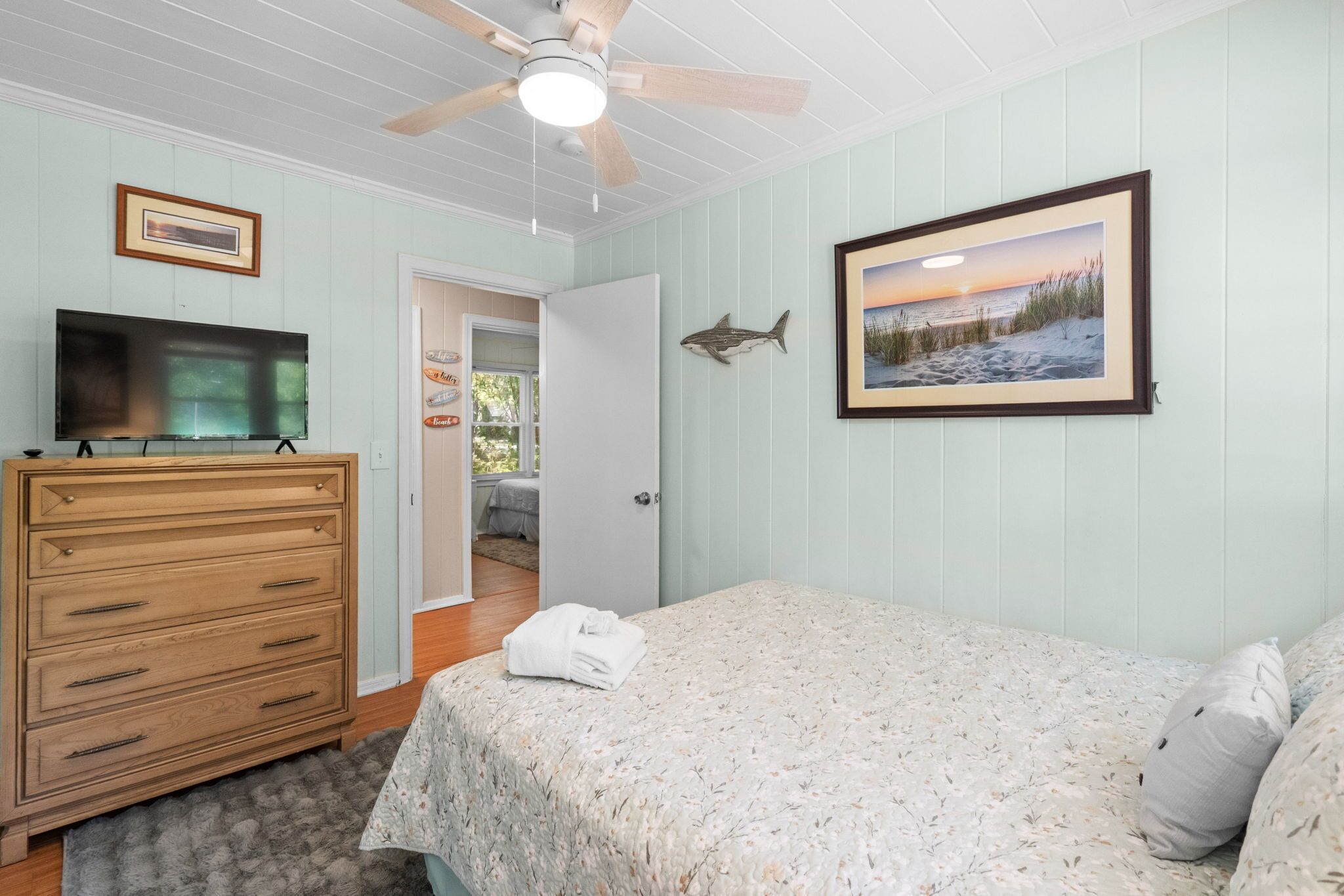 A bedroom with a bed, a dresser, a ceiling fan, a TV, and a framed picture on the wall.