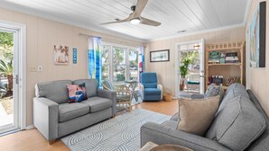 A living room with a grey sofa, a blue armchair, a ceiling fan, and a bookshelf. - Coastal Cottage- 3 Bedroom (Surfside Beach)