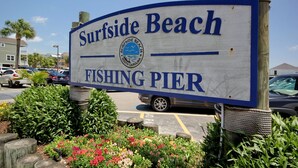 A sign for Surfside Beach Fishing Pier with a clear view of the surrounding parking area and greenery. - Coastal Cottage- 3 Bedroom (Surfside Beach)