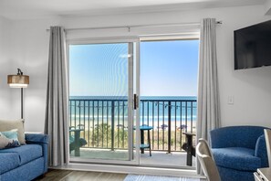 A room with a sliding glass door leading to a balcony with a view of the beach.
