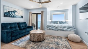 Een moderne slaapkamer met een groot bed, een blauwe bank, een ronde houten salontafel en een plafondventilator.
