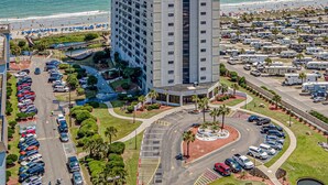 Een hoog hotel met een parkeerplaats en uitzicht op het strand.