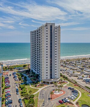 A high-rise hotel with a parking lot and beach view.