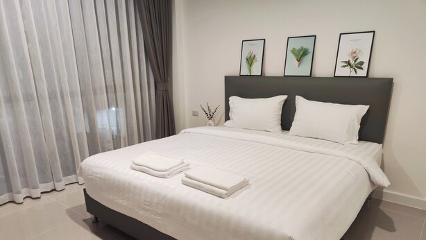 A neatly made bed with white linens and towels, a dark headboard, and three framed botanical prints on the wall. - The Olive House Hotel (Khon Kaen)