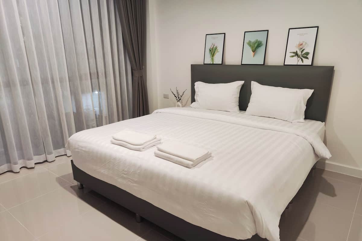 A neatly made bed with white linens and towels, a dark headboard, and three framed botanical prints on the wall.