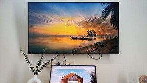 A laptop on a wooden table with a monitor displaying a sunset scene. - The Olive House Hotel (Khon Kaen)