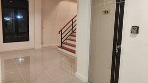A hallway with a polished floor, a door marked with the number 104, and a staircase with a black railing. - The Olive House Hotel (Khon Kaen)