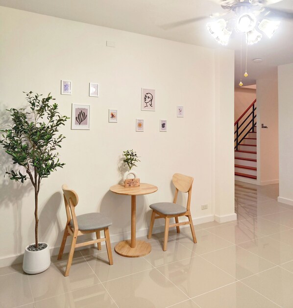 A room with a potted plant, two wooden chairs, a small round table, and wall-mounted artwork. - The Olive House Hotel (Khon Kaen)