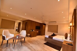 Habitació d'hotel amb un llit, dues cadires, una taula petita, un televisor i un ventilador de sostre.