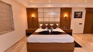 Quarto de hotel moderno com uma cama grande, cabeceira de madeira, duas mesas de cabeceira com abajures, uma janela com persianas e um quadro na parede.