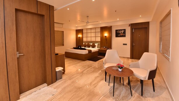 Quarto de hotel moderno com uma cama grande, um espaço para sentar com duas cadeiras, uma mesinha e um banheiro.