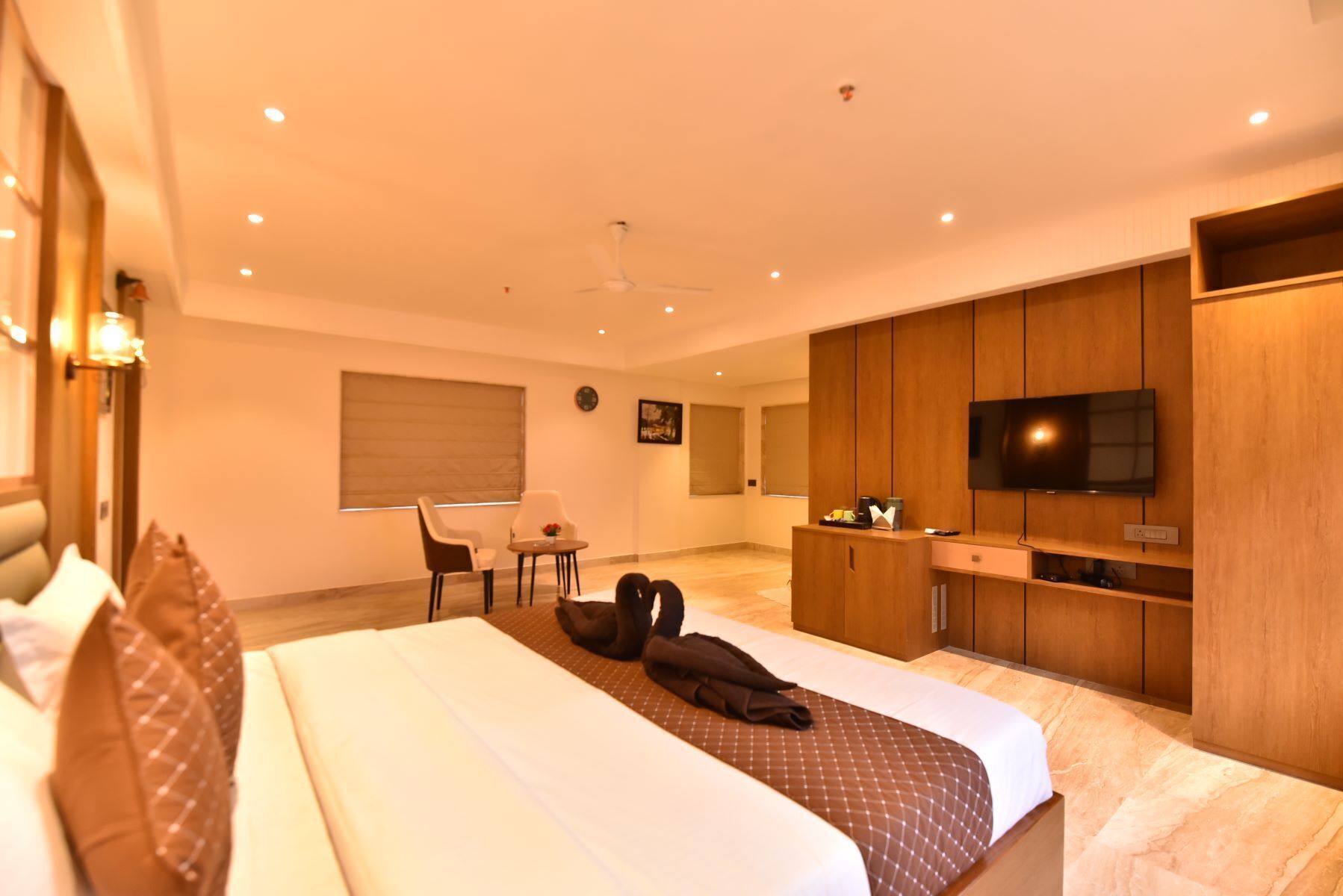 A hotel room with a large bed, a television, a desk with a chair, and a window with blinds.