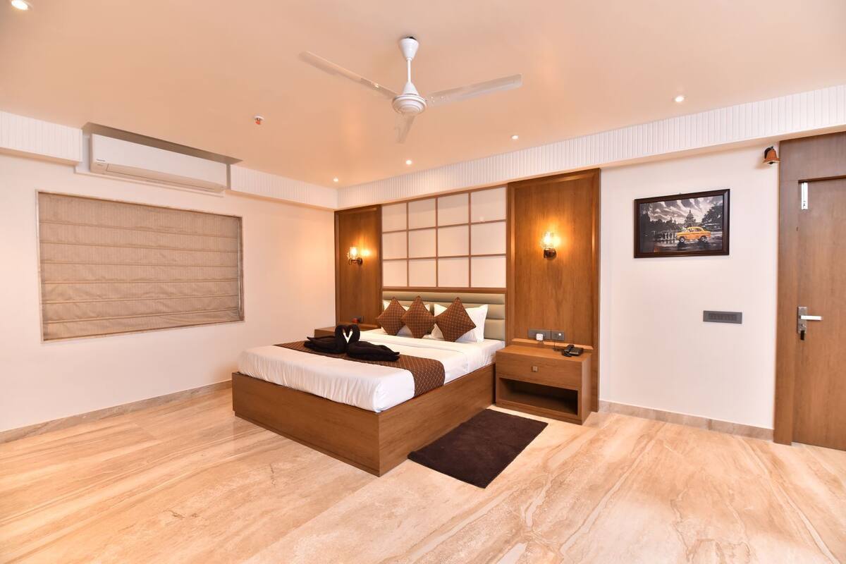 A modern hotel bedroom with a large bed, a ceiling fan, a nightstand, and a wall-mounted light.