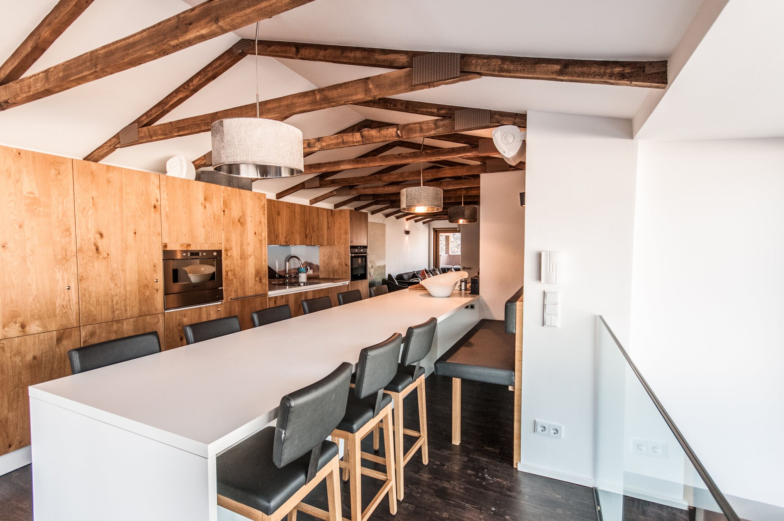 Une cuisine moderne avec des poutres en bois, un grand îlot central et des tabourets de bar.