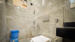 A bathroom with a toilet, a shower, and a blue bucket. - Shri Ram Retreat (Vrindavan)