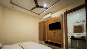 A bedroom with a bed, a ceiling fan, a mounted TV, and a bathroom with a sink and mirror. - Shri Ram Retreat (Vrindavan)