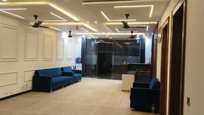 A modern hotel lobby with a blue sofa, a small table, ceiling fans, and recessed lighting. - Shri Ram Retreat (Vrindavan)