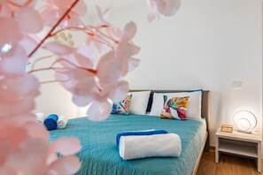 A neatly made bed with a teal bedspread, a white towel, and colorful pillows. There is a small bedside table with a lamp and a mirror. - Terrace- new - 900m Tower -Park priv- spacious (Pisa)
