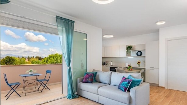 Un soggiorno moderno con divano, tavolo da pranzo con sedie, angolo cottura e balcone con vista.
