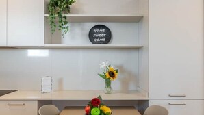 Una cucina con mobili bianchi, un piano di lavoro bianco, un vaso con fiori e frutta esposta.