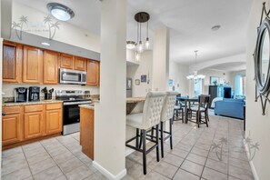 A modern kitchen with wooden cabinets, a built-in microwave, and a dining area with bar stools. - Legacy Tower II 206 | Stunning Coastal Views! (Gulfport)