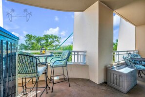 A balcony with outdoor furniture, a glass enclosure, and a view of trees and sky. - Legacy Tower II 206 | Stunning Coastal Views! (Gulfport)