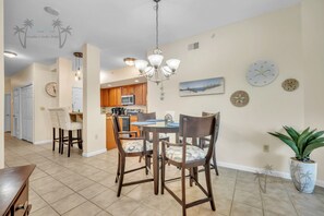 A dining area with a chandelier, wooden chairs, a round table, and a potted plant. - Legacy Tower II 206 | Stunning Coastal Views! (Gulfport)