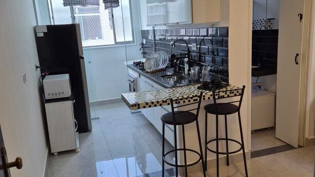 Cozinha compacta com painel de azulejos, uma geladeira pequena e um espaço bar com banquetas.