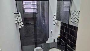 Uma casa de banho moderna com cabine de duche em vidro, sanita branca, lavatório com bancada de granito e um espelho grande.