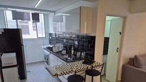 Uma cozinha compacta com ilha central, área de refeições com dois bancos, geladeira e micro-ondas.