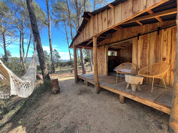 A wooden cabin with a porch, two wicker chairs, and a hammock.