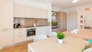 Una cuina moderna amb armaris blancs, forn integrat i zona de menjador amb taula i cadires.