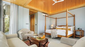 Ein Bett mit Himmelbettgestell aus Holz, eine Sitzecke mit Couchtisch und Blick ins Freie durch große Fenster.