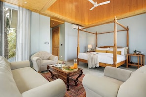 A four-poster bed with a wooden frame, a sitting area with a coffee table, and a view of the outdoors through large windows. - ELIVAAS 4 BHK Kavya Villa With Lounge  (Kasauli)