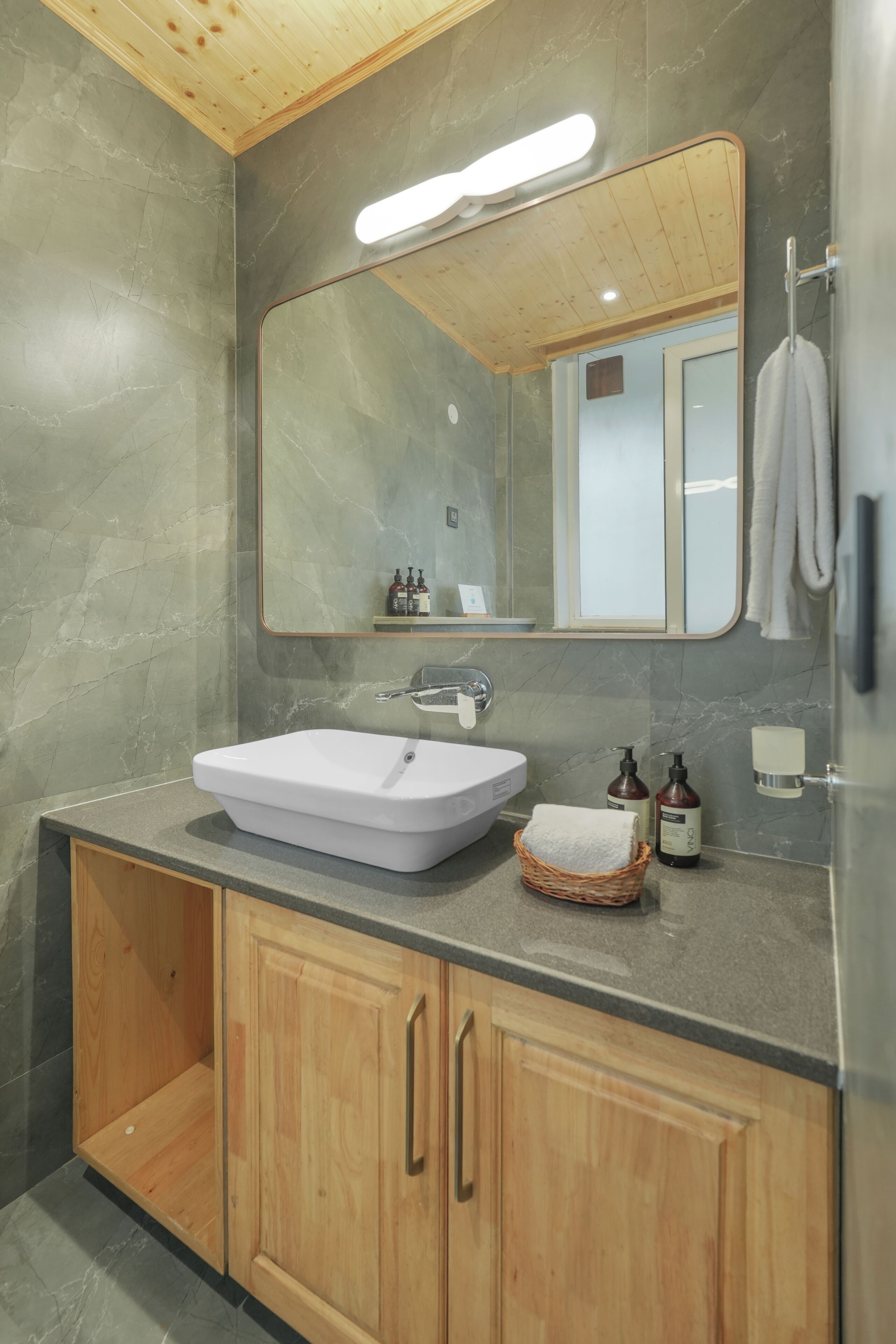 A bathroom with a white sink, wooden cabinets, a mirror, and a towel rack.
