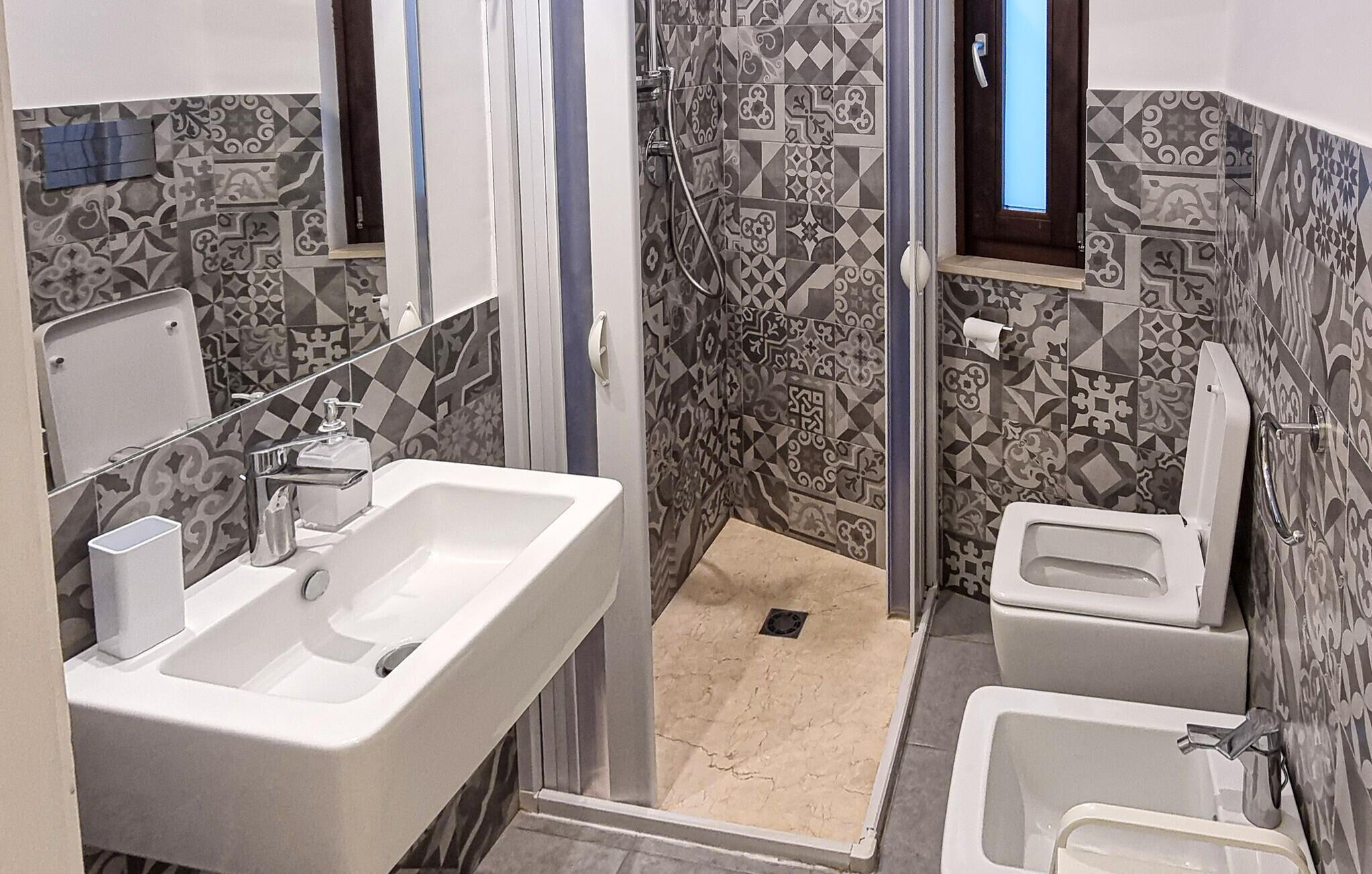 Ein Badezimmer mit einem weißen Waschbecken, einem Spiegel, einer Dusche und einer Toilette.