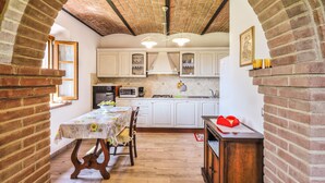 Een keuken met witte kasten, een bakstenen boog en een eettafel met stoelen.