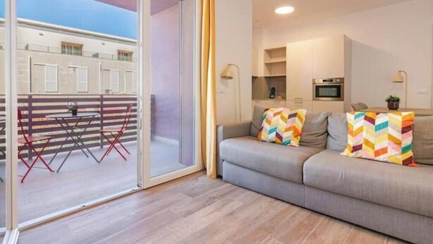 Un salon moderne comprenant un canapé, des coussins colorés, un coin repas avec une table et des chaises, et un coin cuisine avec un four à micro-ondes.