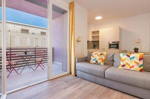 A modern living room with a sofa, colorful pillows, a dining area with a table and chairs, and a kitchen area with a microwave. - Apartment with Balcony - 900 m from Tower, Private Park & Modern Comfort (Pisa)