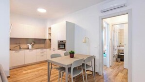 Une cuisine moderne avec des meubles blancs, une table à manger avec des chaises et une petite plante posée sur la table.