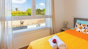 Une chambre d’hôtel avec un lit, une fenêtre donnant sur un paysage verdoyant et une table de chevet avec une lampe.