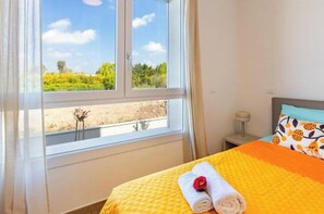 A hotel room with a bed, a window with a view of greenery, and a nightstand with a lamp. - Apartment with Balcony - 900 m from Tower, Private Park & Modern Comfort (Pisa)