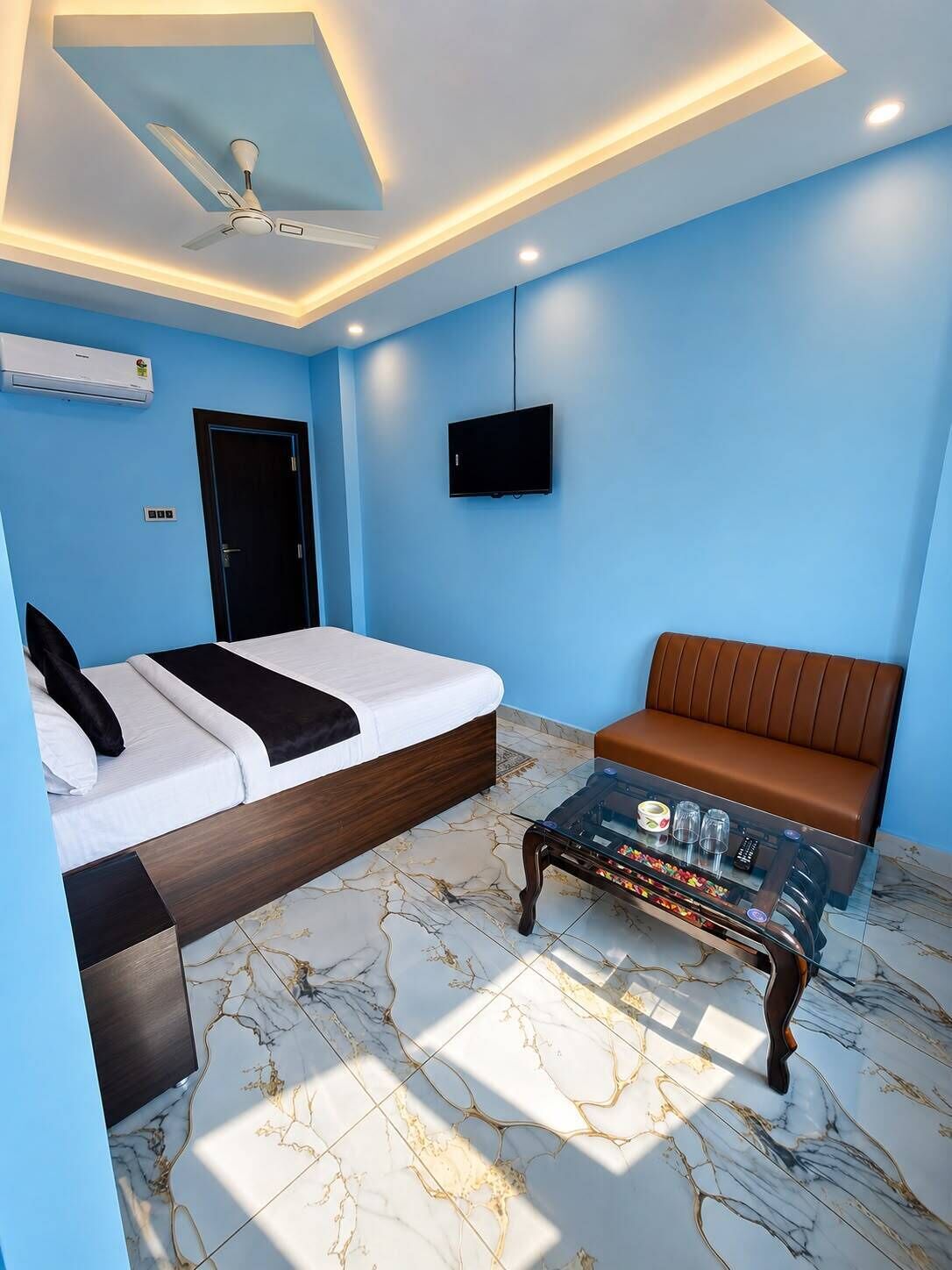 A hotel room with a bed, a sofa, a coffee table, a television, and a ceiling fan.