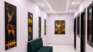 A hallway with a green sofa, framed artwork on the walls, and a marble floor. - Hotel 5G (Bhopal)