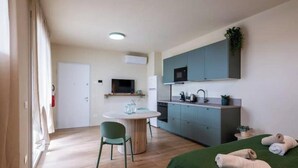 Une pièce compacte comprenant un lit, une petite table à manger, un coin cuisine et un téléviseur.