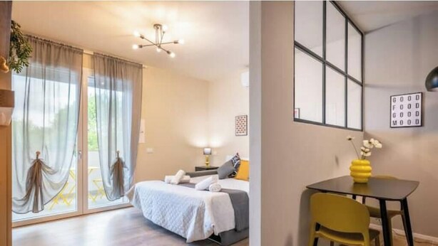 Ein Schlafzimmer mit Bett, Nachttisch, Lampe, Vorhängen und Blick durch das Fenster.