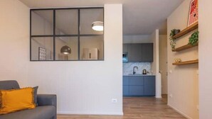 Ein Wohnzimmer mit einer Couch, einem Fenster und einer Küche im Hintergrund.