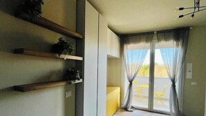 A room with a sliding door leading to an outdoor area, a wooden floor, and built-in shelves with decorative items. - New Apartment with Balcony - Near Tower, Private Park (Pisa)