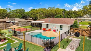 Un jardin avec une piscine, un terrain de basket et un espace patio couvert.