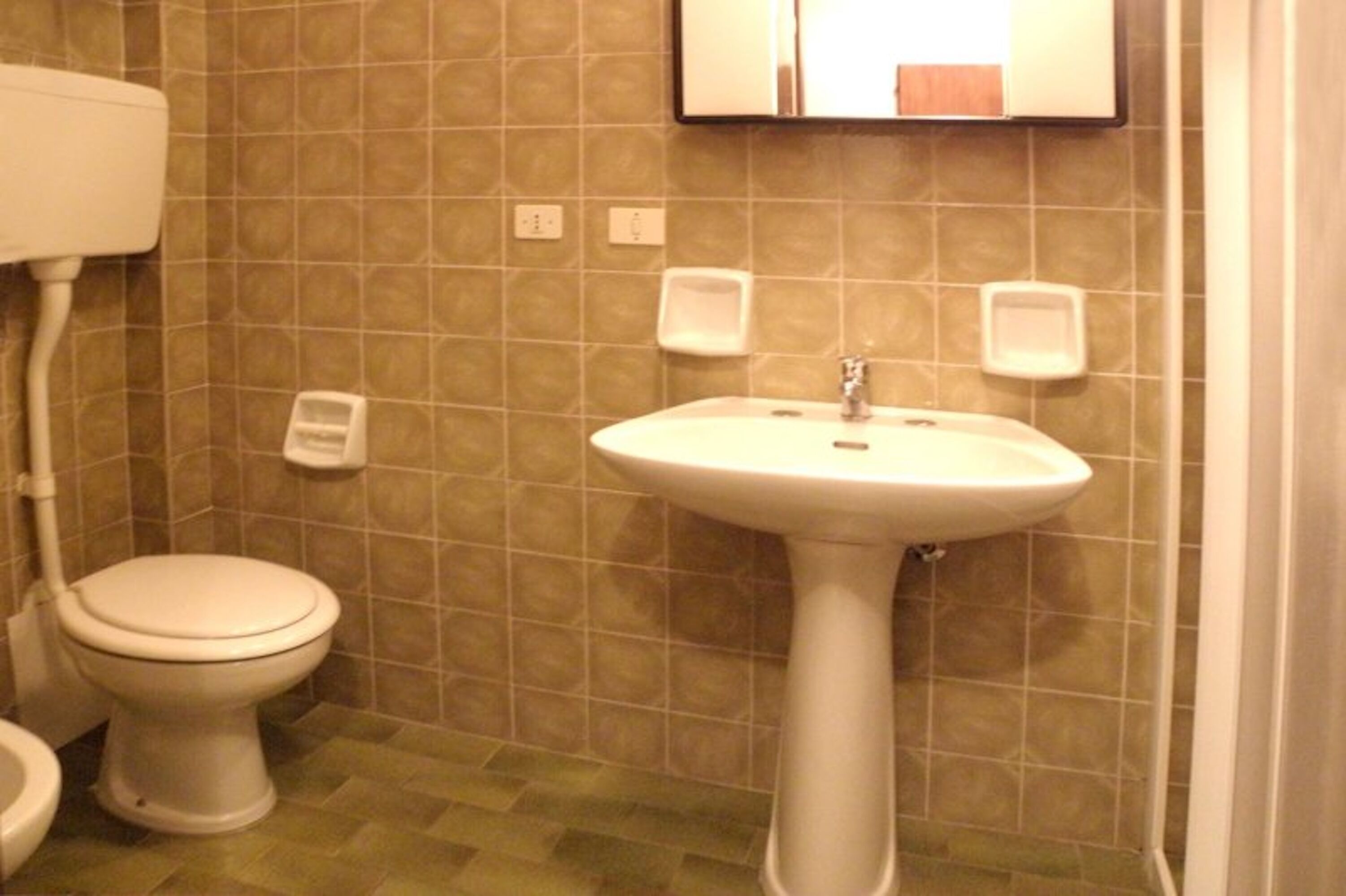 Un bagno con il water, un lavandino e due erogatori di sapone a parete.